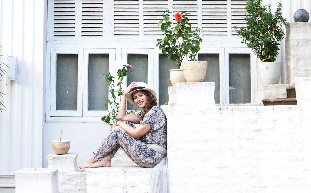 Linden Schaffer sitting on whitewashed steps in a sun hat
